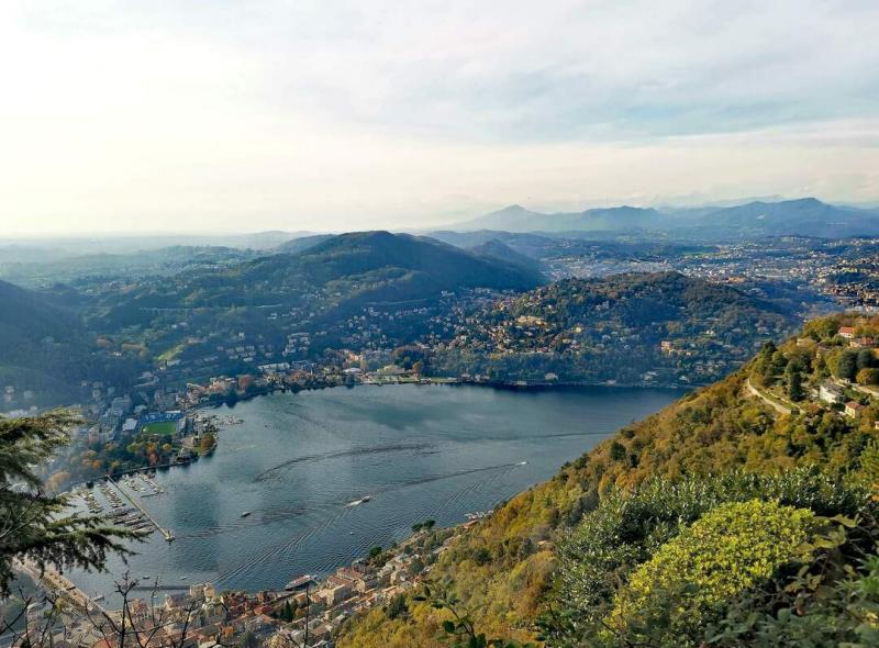 A késő őszi napfény lágyan simogatja a Comói-tó partjait, ahol a lombardiai táj festői szépsége bámulatba ejti az arra látogatókat. A fák levelei már csak néhány színpompás árnyalatot viselnek, a sárgától a vörösig terjedő paletta varázslatos kontrasztot 